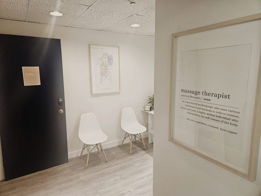 Inviting waiting room at Soma Massage and Wellness with comfortable seating, soft lighting, and calming decor including green plants and neatly arranged magazines.